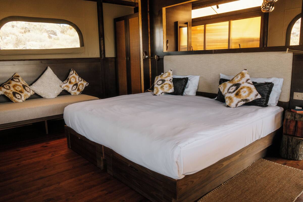 Ein Bett mit Kopfteil, eine Sitzbank mit Kissen, ein Holzboden und ein Fenster mit Blick.