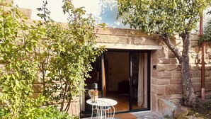 Un patio con una mesa y sillas, una puerta que da al interior y un muro de piedra.