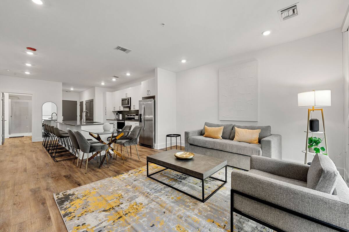 A modern living room with a grey sofa, a coffee table, and a dining area with chairs and a table.
