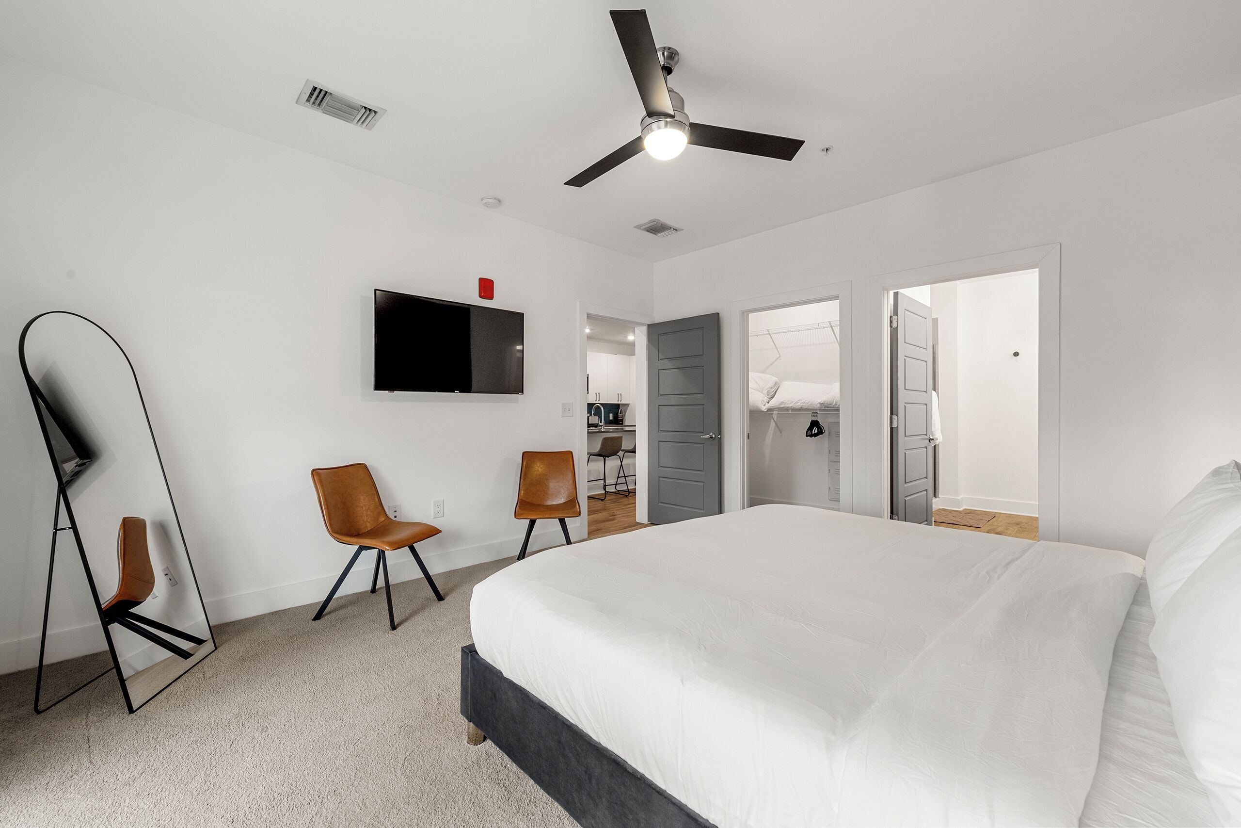 A modern hotel room with a large bed, two chairs, a TV, and a ceiling fan.