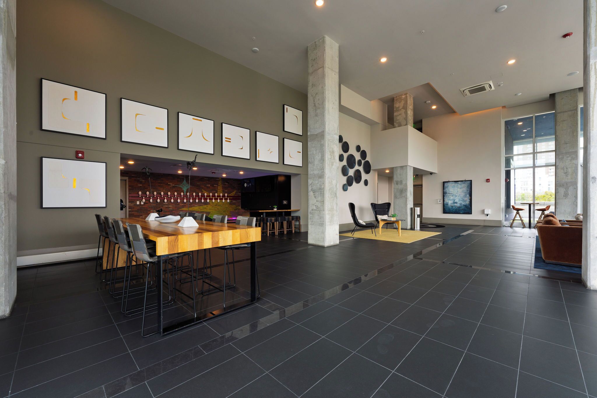 Eine großzügige Lobby mit einem langen Holztisch, mehreren Stühlen, einer Bar und einer Sitzecke mit einer Couch und Sesseln.