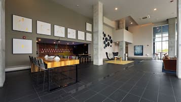 Eine großzügige Lobby mit einem langen Holztisch, mehreren Stühlen, einer Bar und einer Sitzecke mit einer Couch und Sesseln.