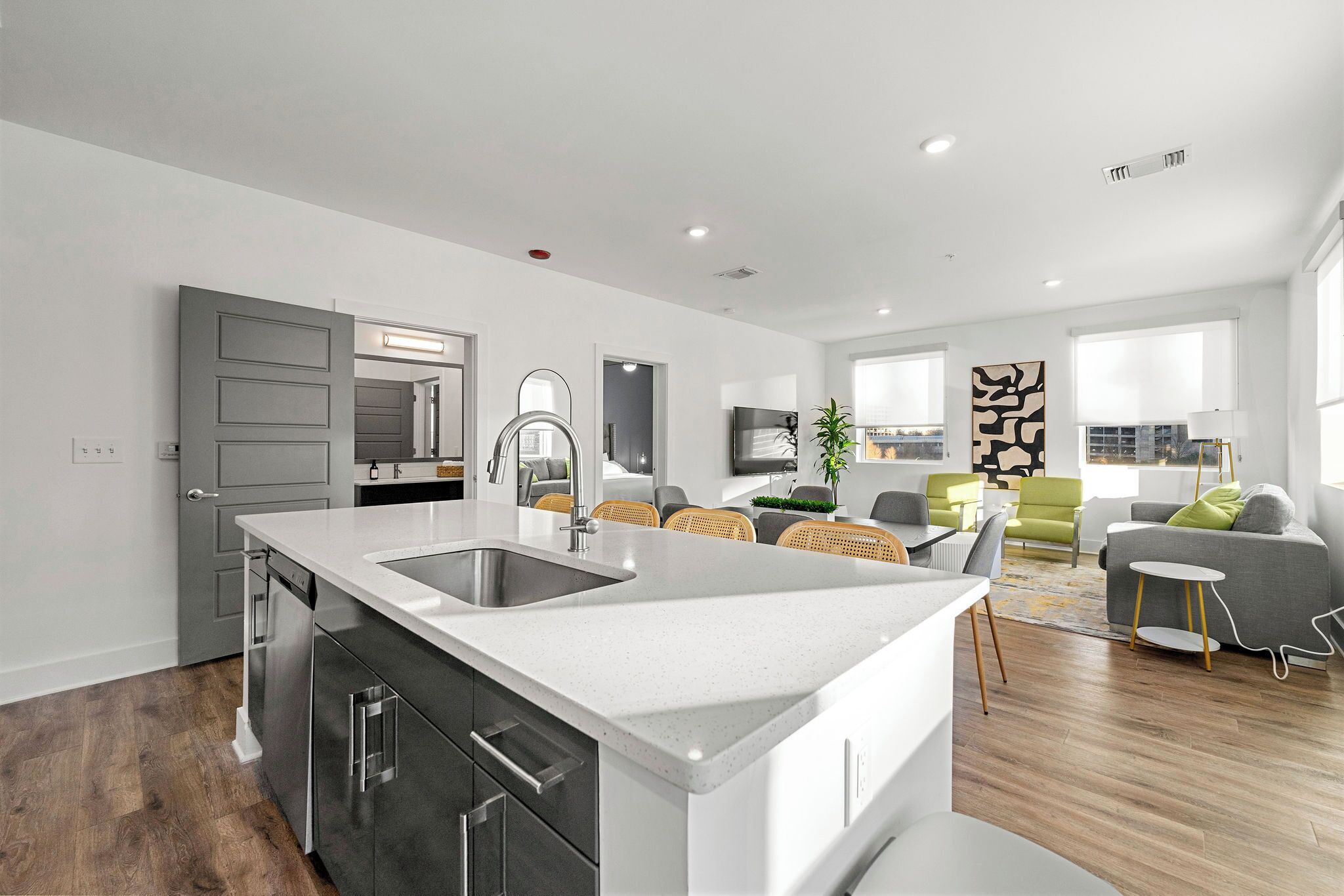 Una cocina moderna con una isla grande, un comedor con una mesa y sillas pequeñas, y una sala de estar con sofá y mesa de centro.