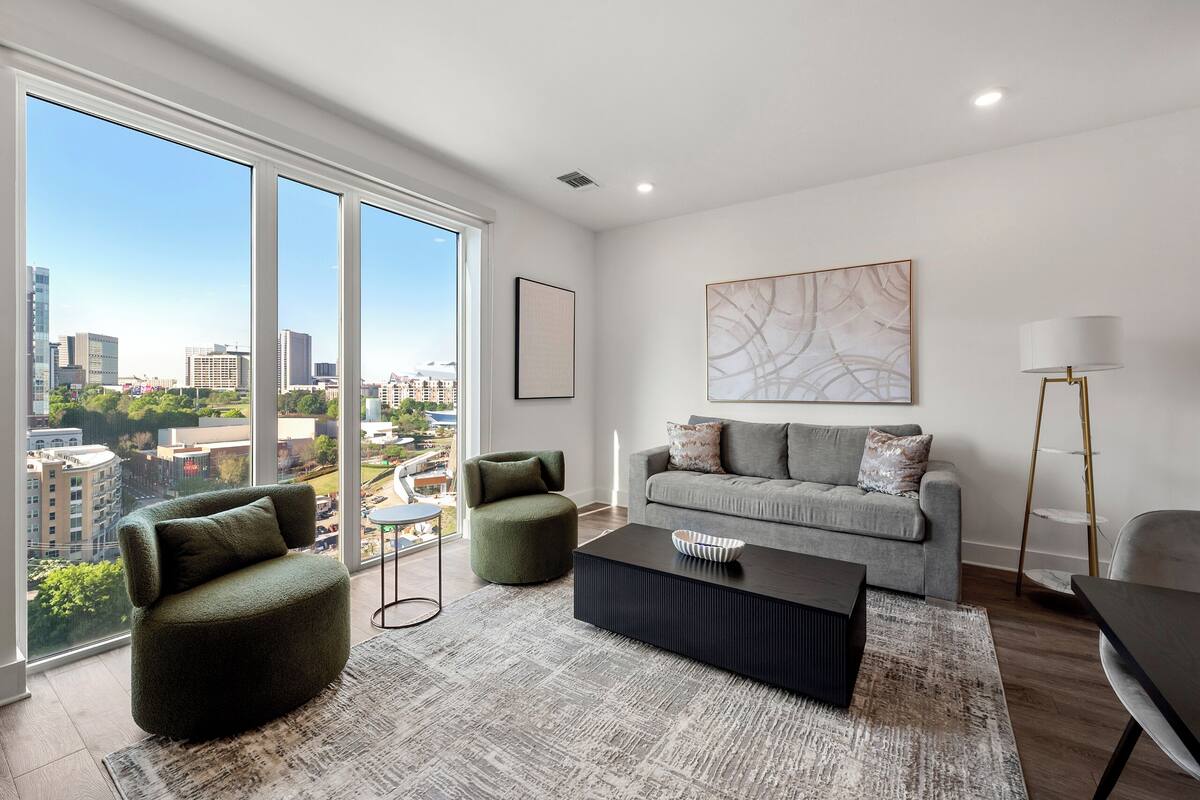 A modern living room with a large window, a grey sofa, a green armchair, a black coffee table, and a floor lamp.