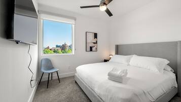 Une chambre d’hôtel moderne dotée d’un grand lit, d’un ventilateur de plafond, d’un téléviseur fixé au mur, d’une chaise et d’une fenêtre donnant sur la ville.