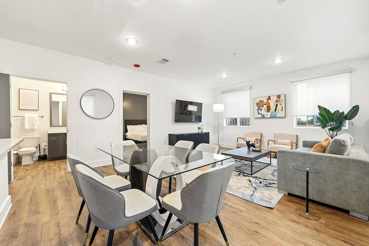 A modern living room with a glass dining table, grey chairs, a grey sofa, and a coffee table.