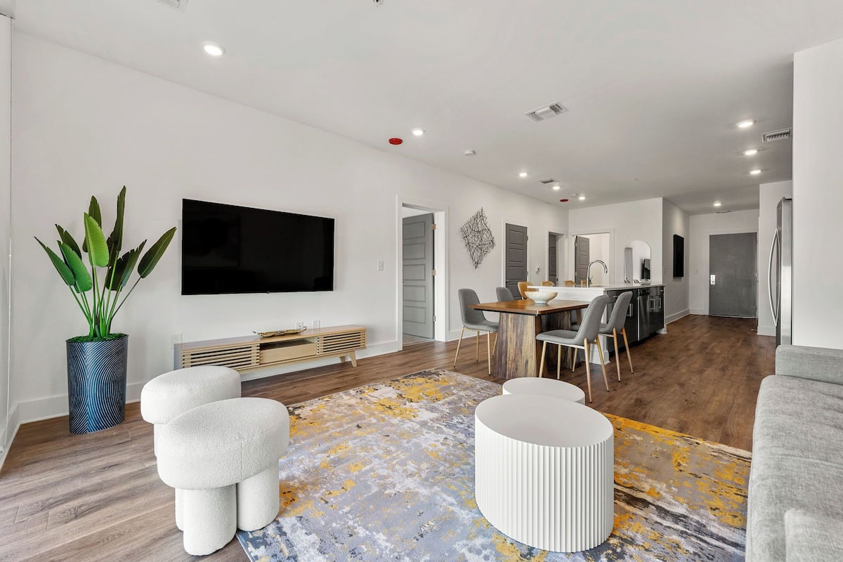 A modern living room with a flat-screen TV, a dining area, and a kitchen.