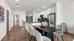 Een moderne keuken met een centraal eiland, witte kasten, roestvrijstalen apparatuur en een eethoek met grijze stoelen.