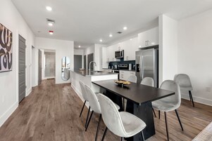 A modern kitchen with a central island, white cabinetry, stainless steel appliances, and a dining area with grey chairs.