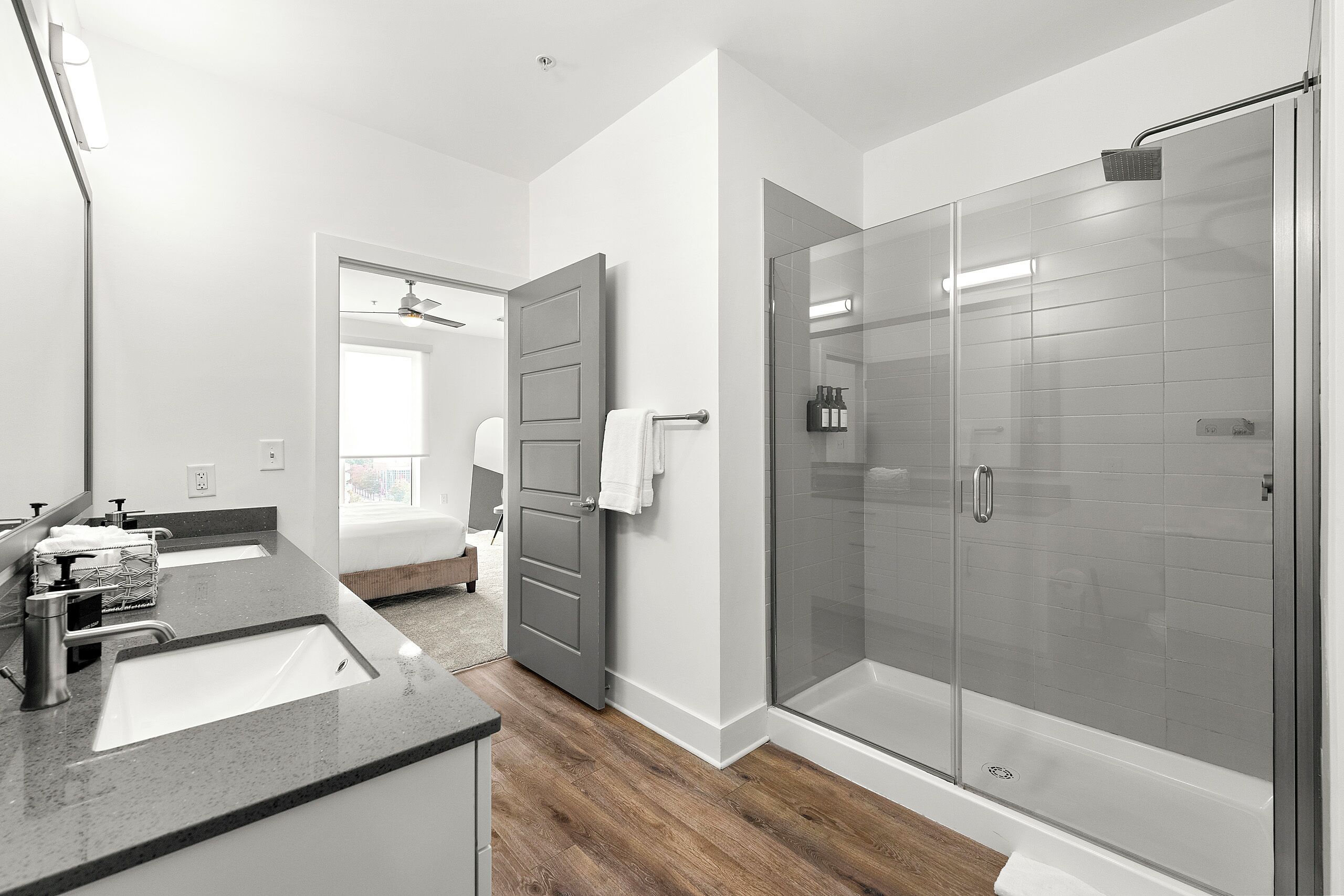 Un baño moderno con cabina de ducha de vidrio, tocador con lavamanos y puerta que da a otra habitación.