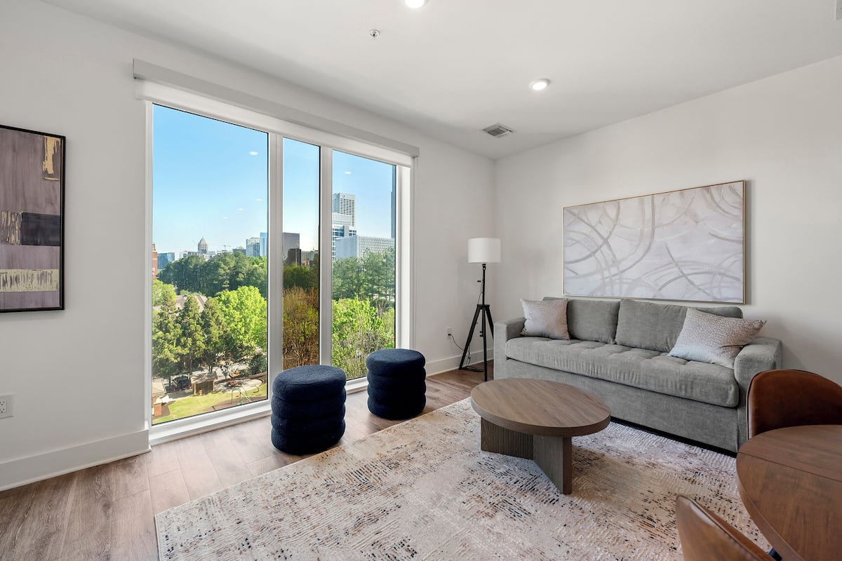 A modern living room with a large sliding glass door, a grey sofa, a round coffee table, and a floor lamp.