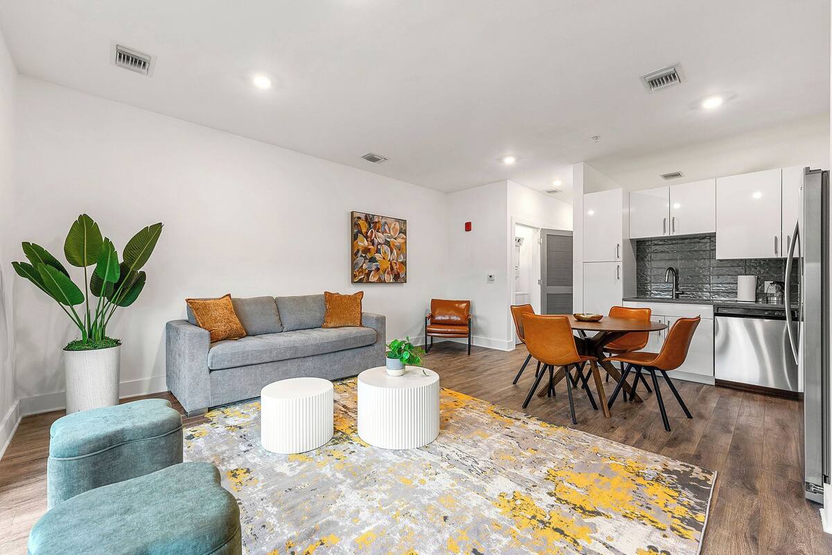 A modern living room with a grey sofa, a coffee table, and a dining area with a table and chairs.