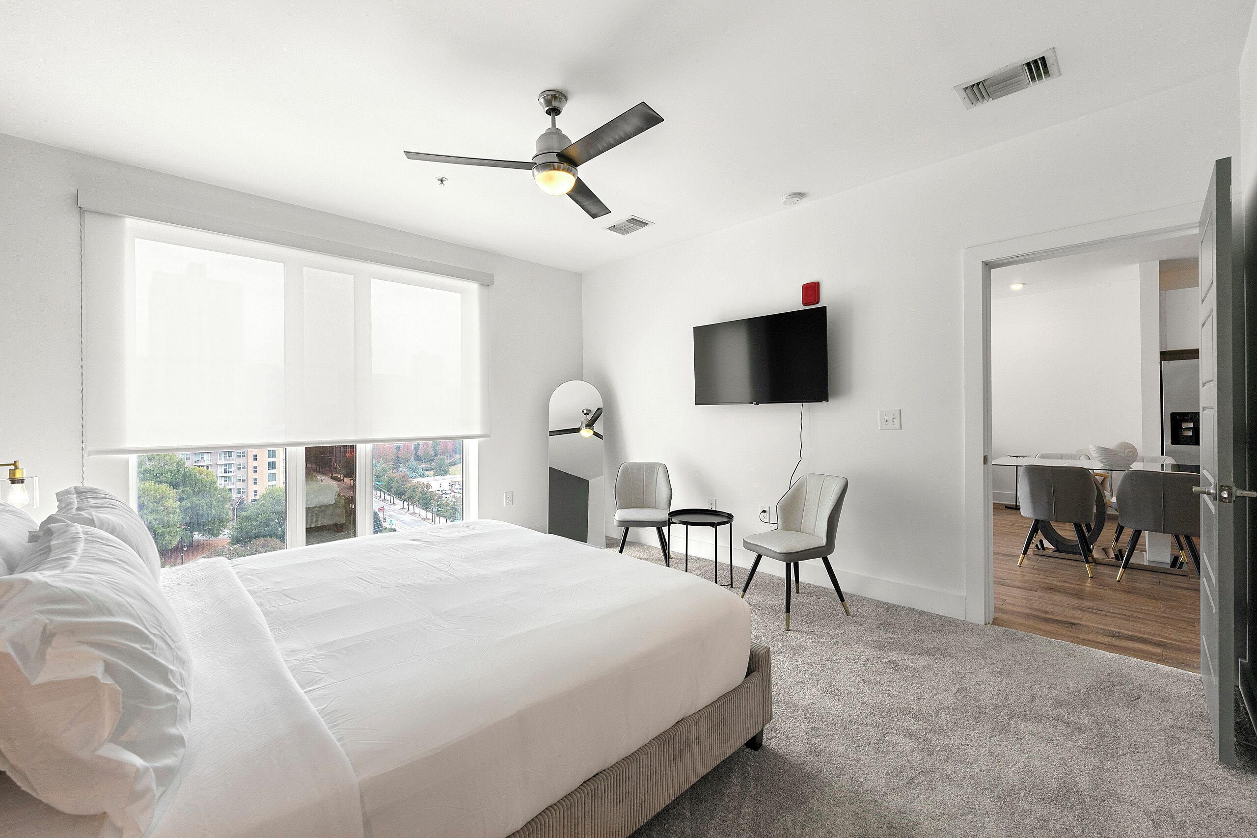 Une chambre moderne avec un grand lit, un ventilateur de plafond, une télévision et une vue sur la ville grâce à de grandes fenêtres.