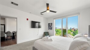 Een moderne slaapkamer met een groot bed, een plafondventilator, een televisie en uitzicht op de stad.