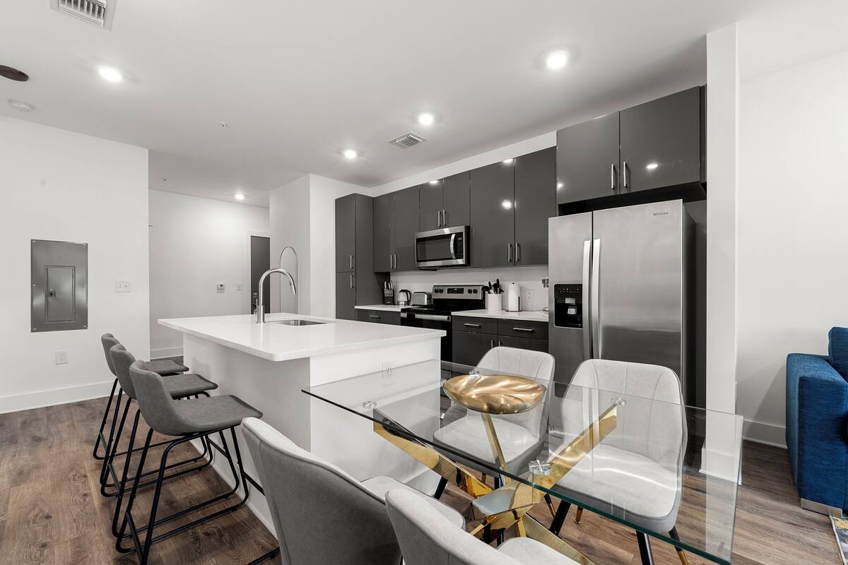 A modern kitchen with dark cabinets, stainless steel appliances, and a glass dining table with chairs.