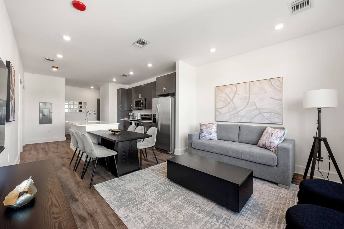 A modern living room with a gray sofa, a coffee table, and a dining area with a dark wooden table and chairs.