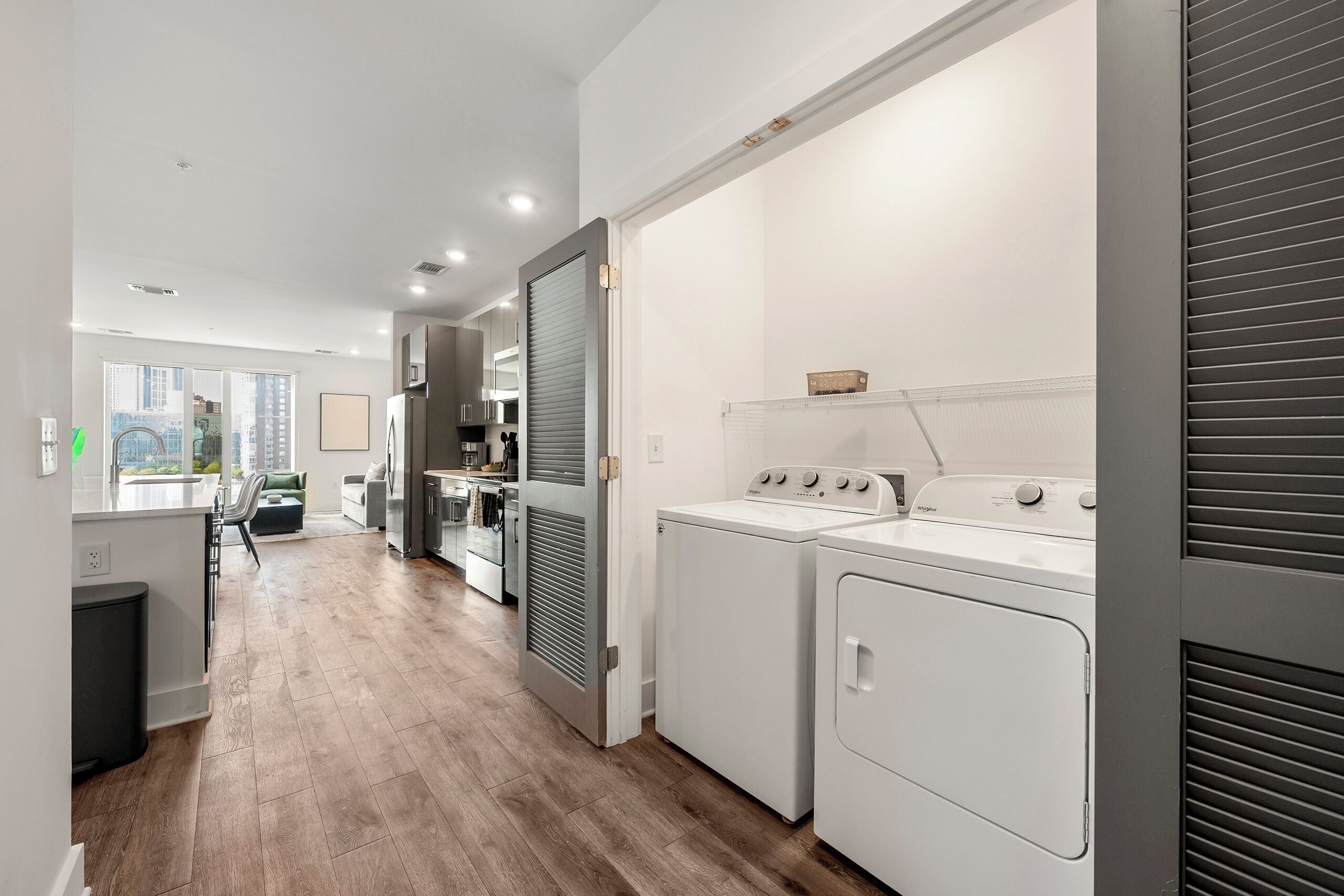 A modern laundry room with a washing machine and dryer, a countertop with a sink, and a view of the city through large windows.