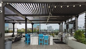 Een terras buiten met een barbecue, blauwe barstoelen en uitzicht op de stadsgezicht.