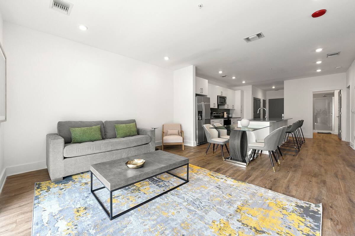 A modern living room with a grey sofa, a coffee table, and a dining area with chairs and a table.