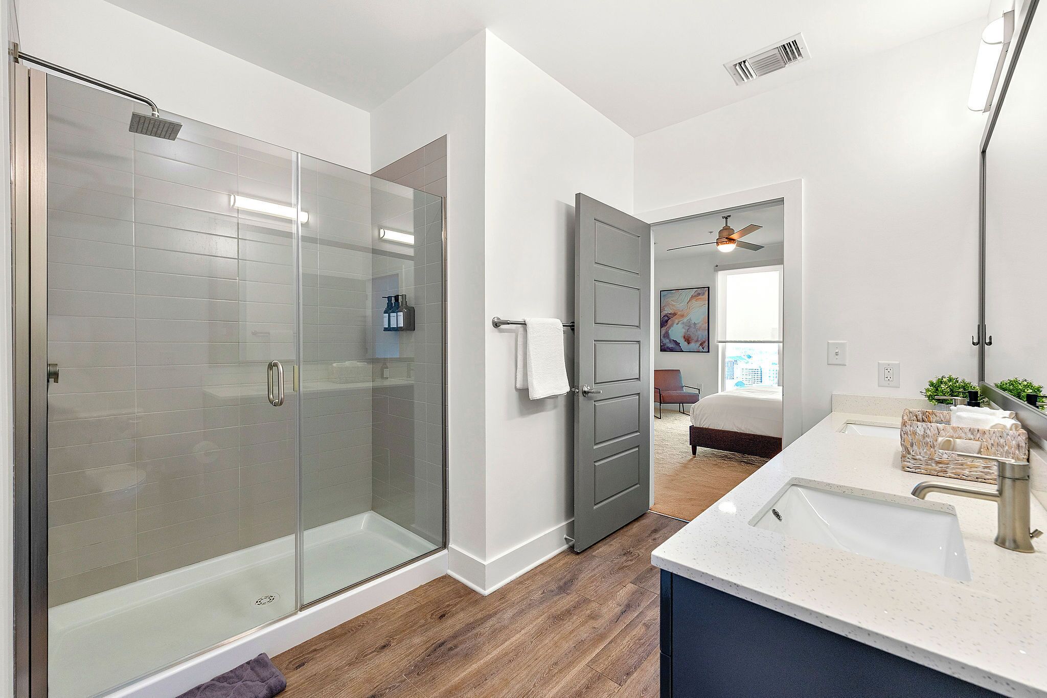 Une salle de bain moderne avec une douche à parois de verre, un meuble-lavabo et une porte donnant sur une chambre.
