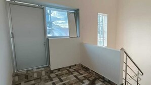 A hallway with a tiled floor, a door, a window, and a metal railing.