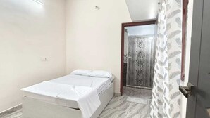 A small, single-bed room with a simple design, a door with a decorative pattern, and a patterned curtain.
