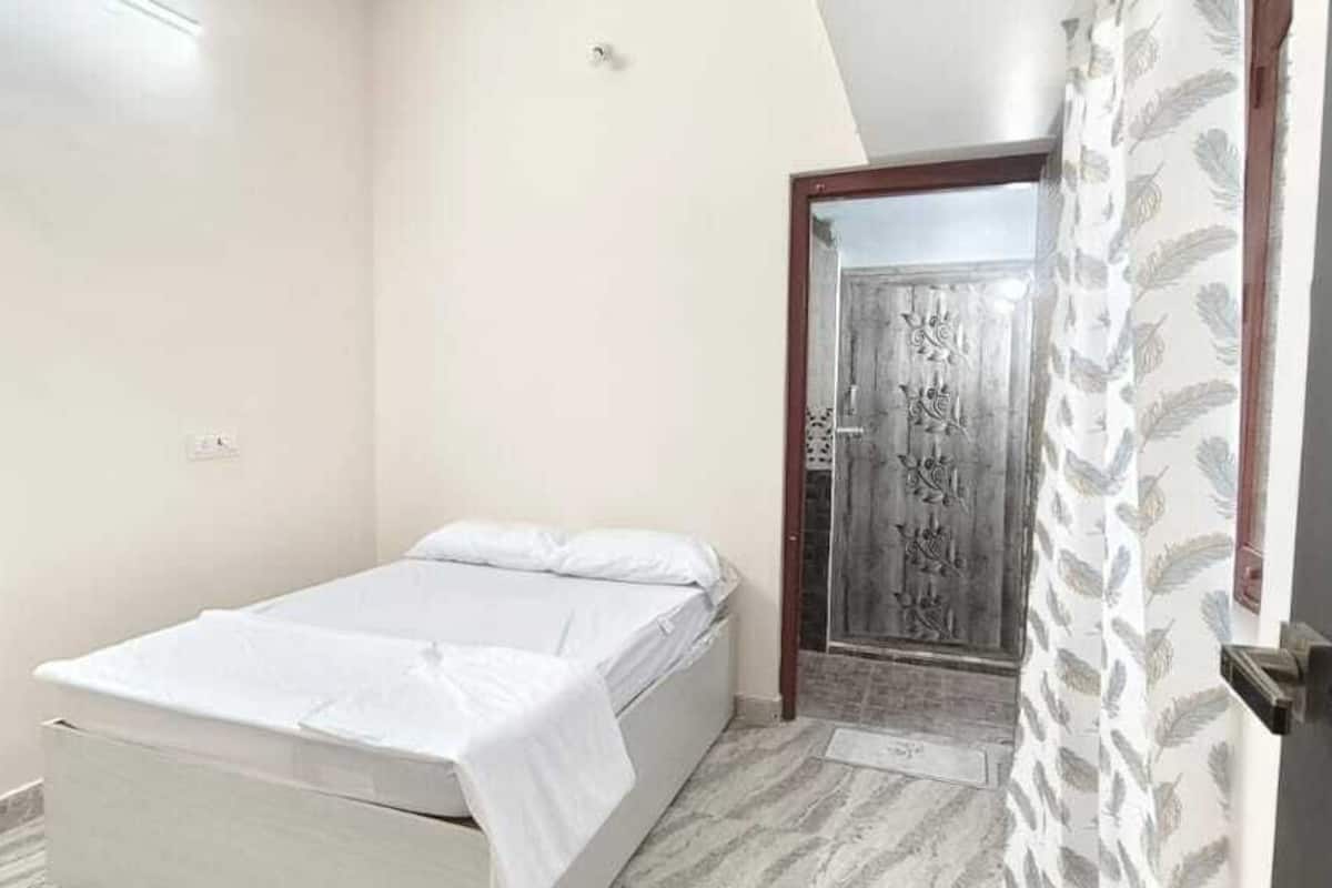A small, single-bed room with a simple design, a door with a decorative pattern, and a patterned curtain.