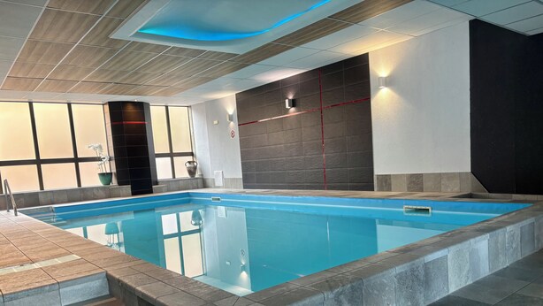 Una piscina interior amb aigua cristal·lina, parets de rajola i un disseny modern.