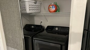 Ein Waschbereich mit zwei Waschmaschinen und Trocknern, einem Wäschekorb und Tide Waschmittel auf einem Regal.