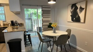 Eine moderne Küche mit einer Granit-Arbeitsplatte, einem Essbereich mit rundem Tisch und Stühlen sowie einer schwarzen Mülltonne.