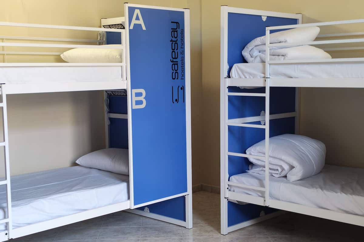 Des lits superposés avec une séparation bleue portant les lettres « A » et « B », dans une pièce dont le sol est recouvert de carreaux.