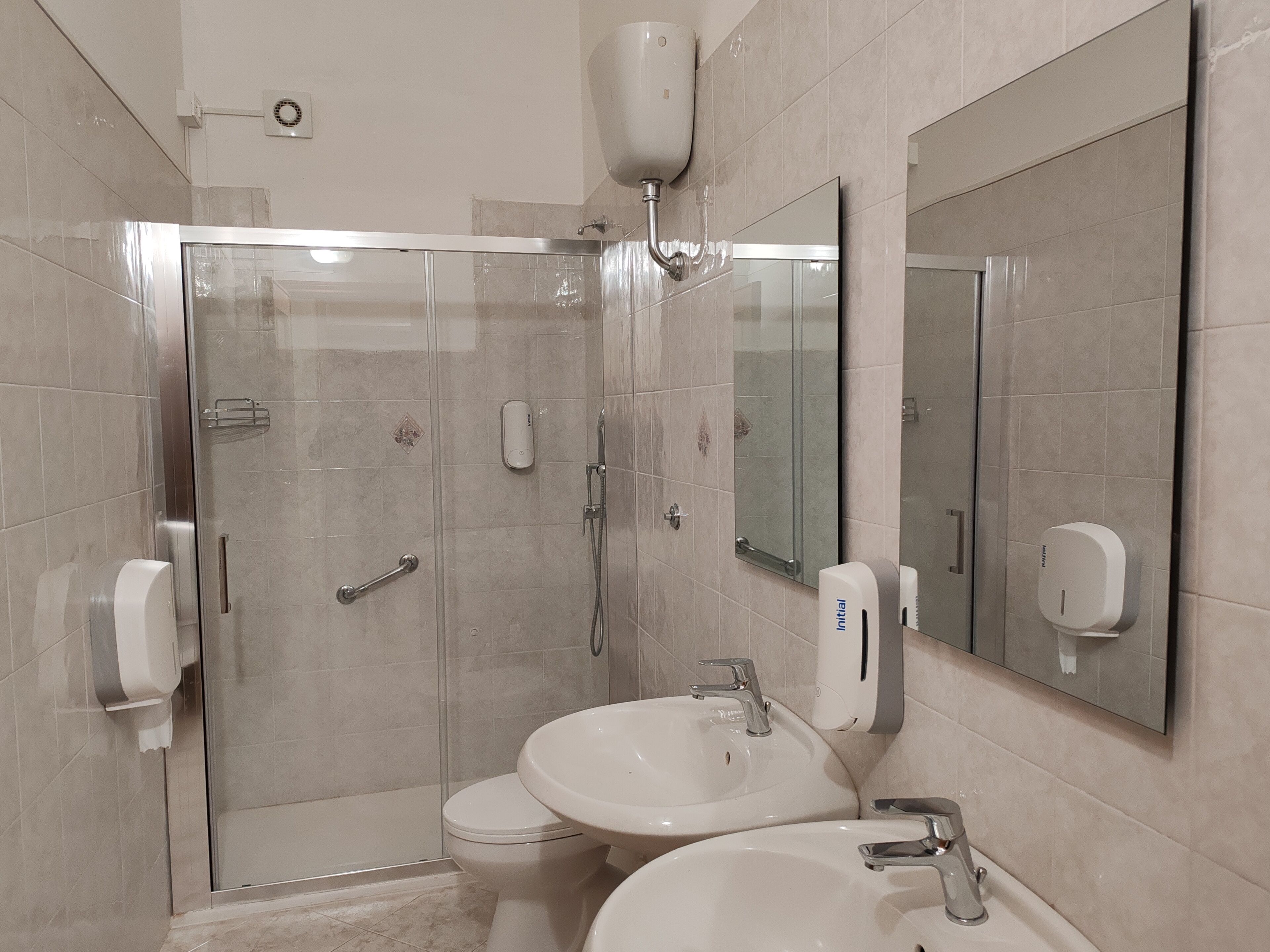 Une salle de bain moderne avec une douche à parois de verre, deux lavabos, des toilettes et un grand miroir.