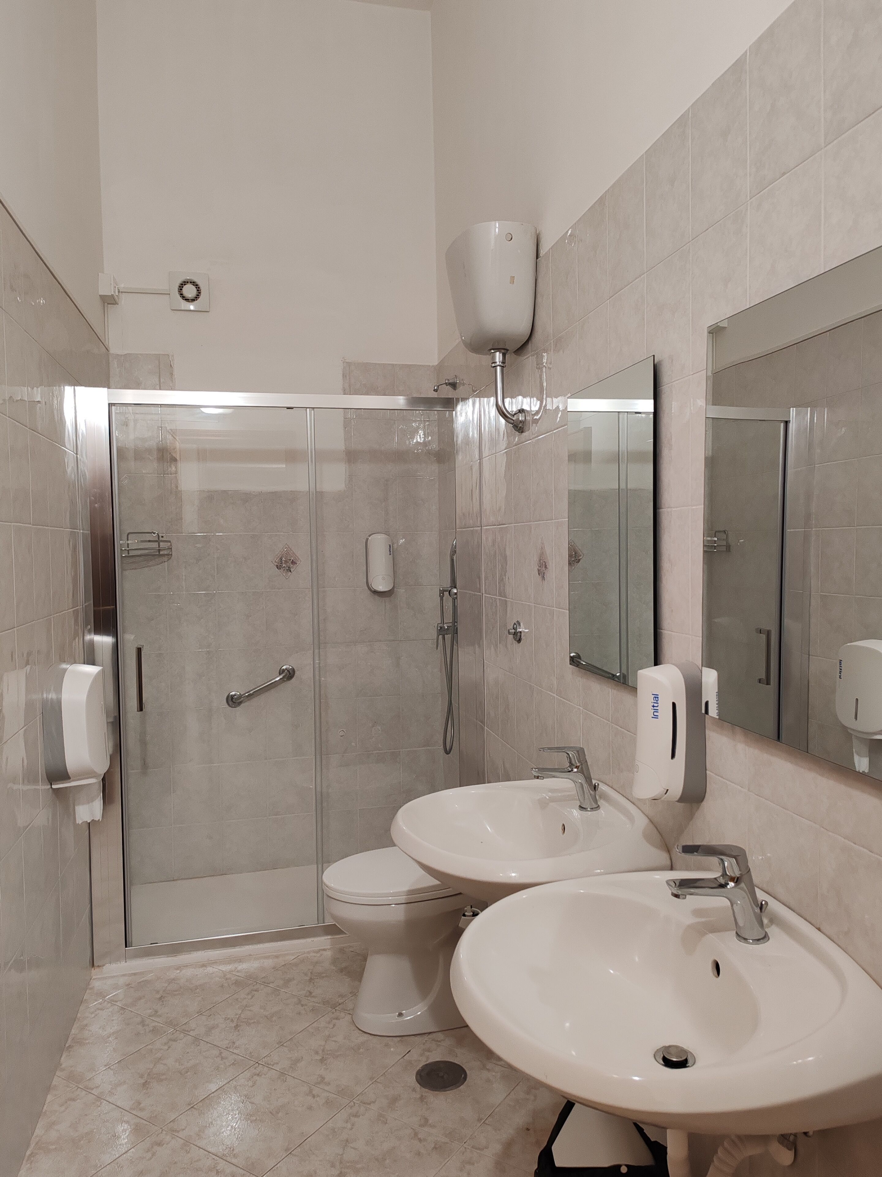 A modern bathroom with a glass-enclosed shower, two sinks, a toilet, and a large mirror.