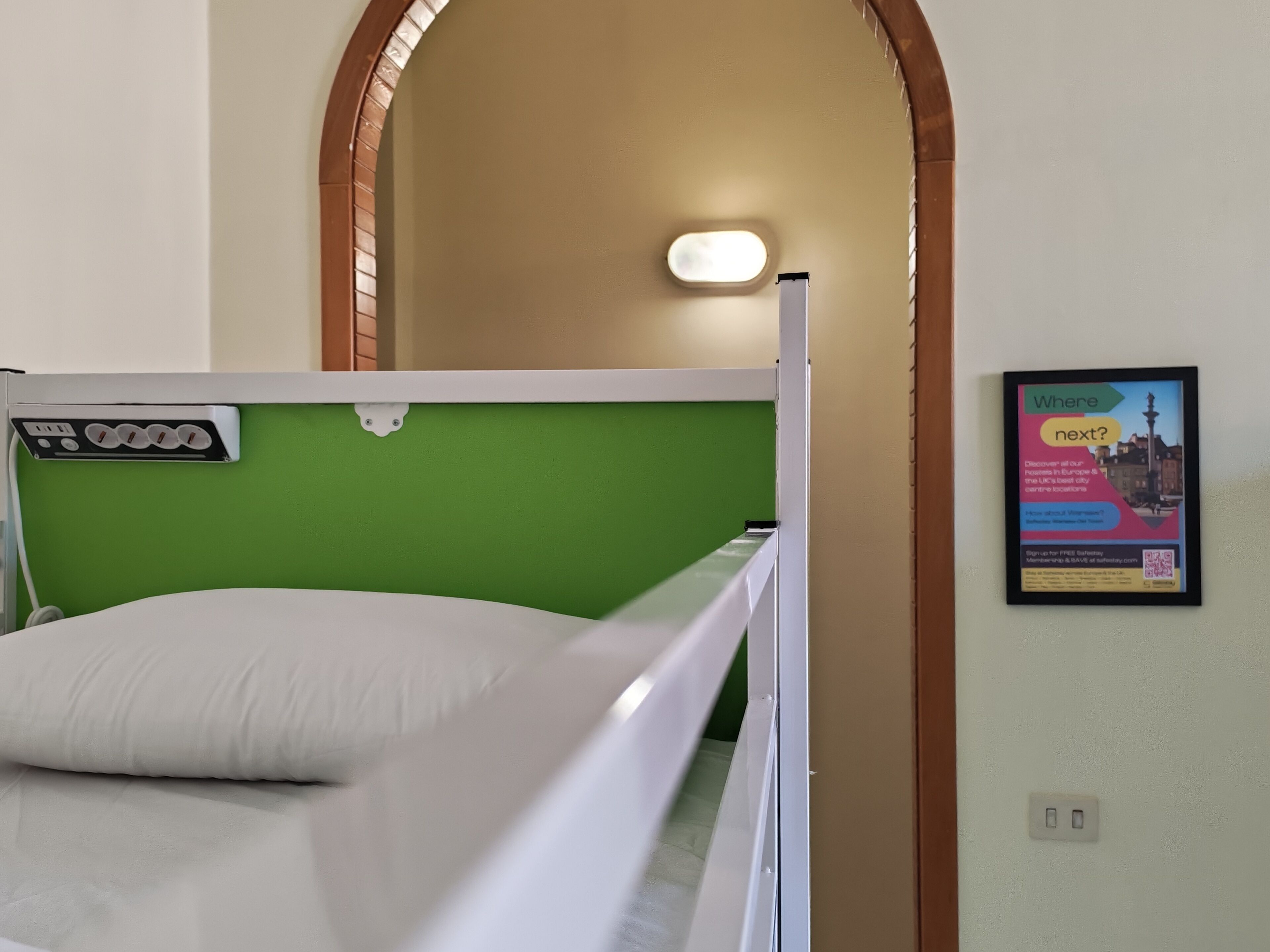 A bunk bed with a green headboard, a wall-mounted light, and a framed informational poster.