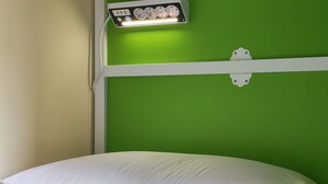 A bed with a white pillow, a green wall, and a power strip with a light. - Safestay Naples Materdei (Naples)