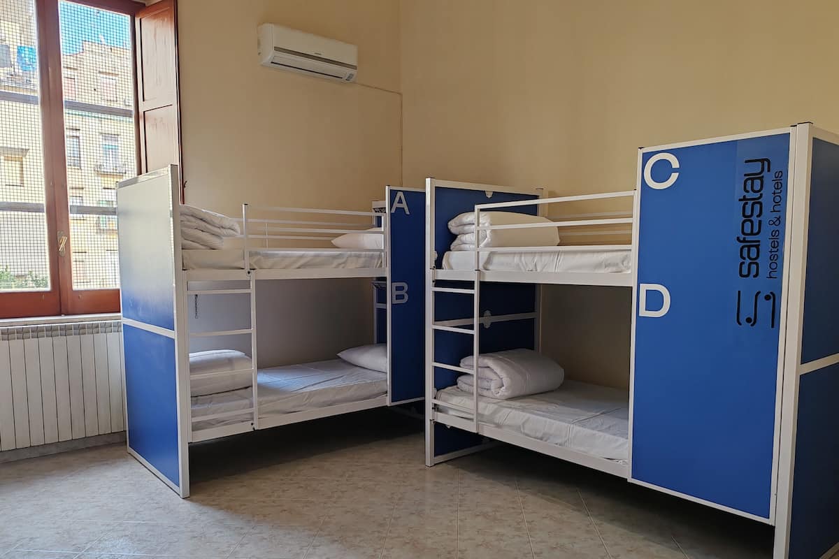Dans une chambre équipée d’une fenêtre, d’un radiateur et d’un appareil de climatisation, on trouve des lits superposés étiquetés A, B, C et D.