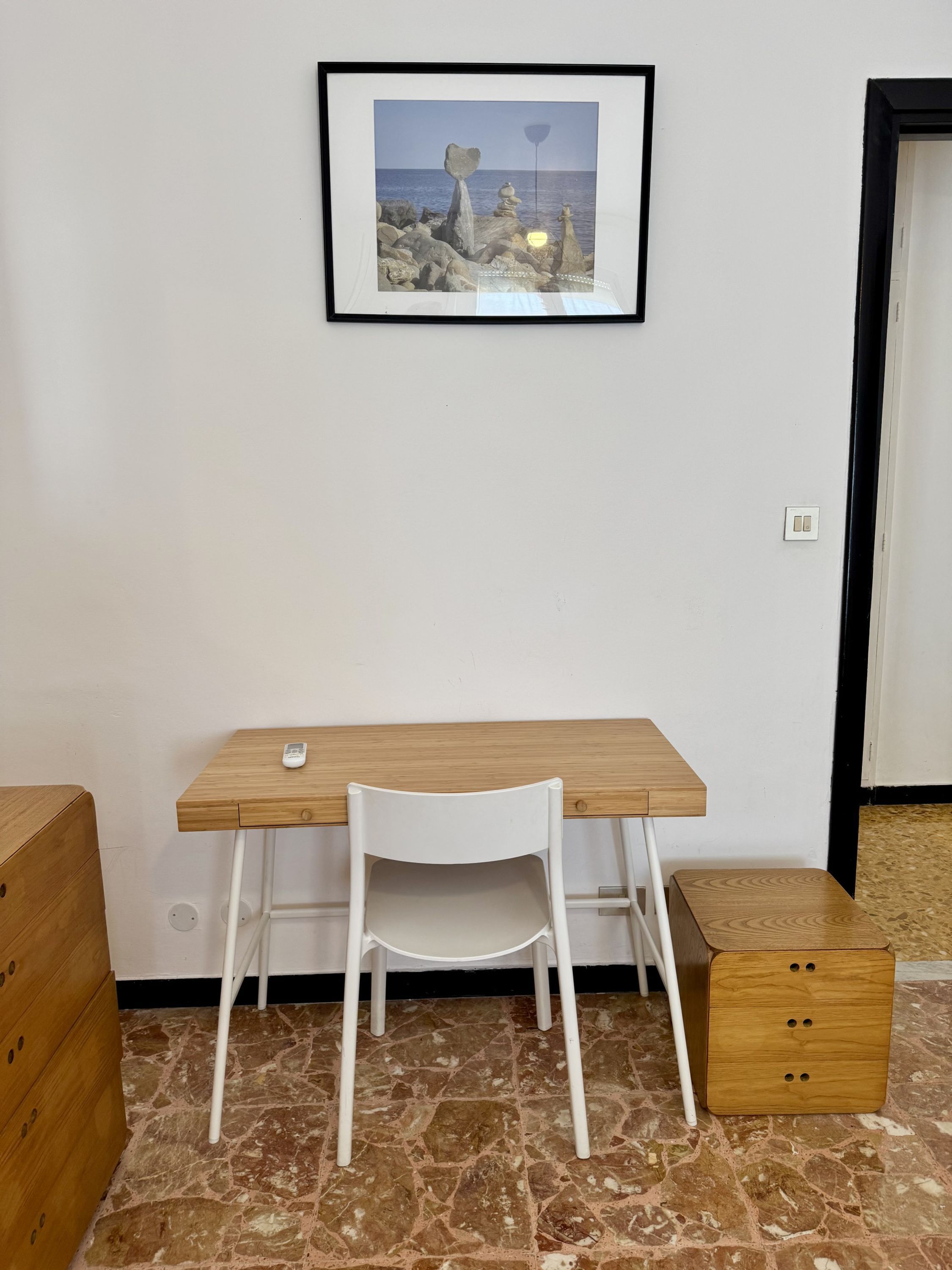 Una habitación pequeña con un escritorio de madera, una silla blanca y un cuadro en la pared.