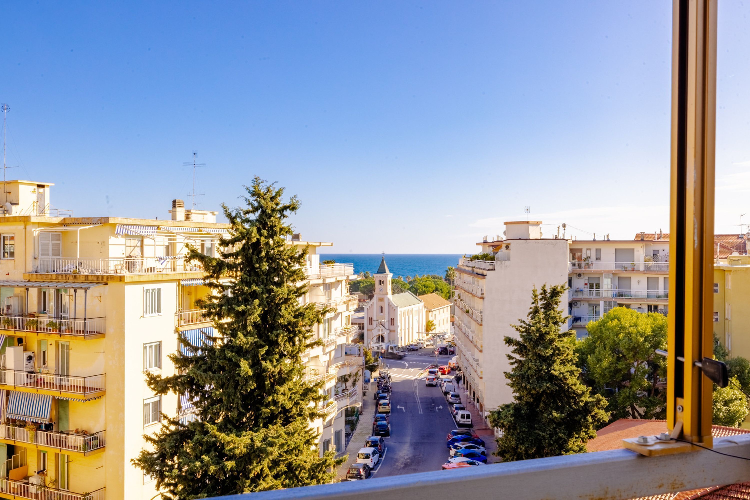 A street view with buildings, parked cars, and a clear sky.