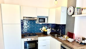 Eine moderne Küche mit weißen Schränken, einer blauen Fliesenspiegel, einem Gasherd, einem Backofen, einer Mikrowelle, einer Spüle und einer Kaffeemaschine.