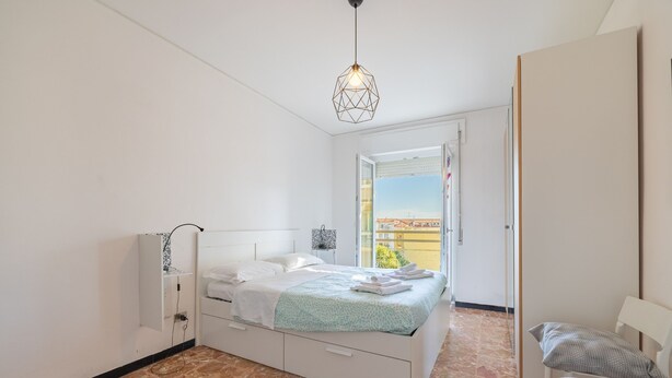 Ein Schlafzimmer mit einem Bett, einem weißen Wandschrank, einem Fenster mit Blick und einer Pendelleuchte.