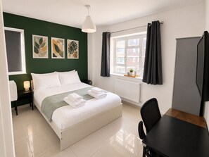 Hotelkamer met een bed, bureau, stoel, raam met gordijnen en kunst aan de muur.