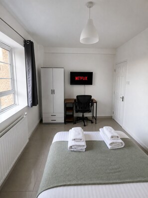 Une chambre d’hôtel avec un lit, un bureau, une chaise, une télévision et une fenêtre.