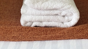 A rolled white towel on a brown textured mat, placed on a white bed.