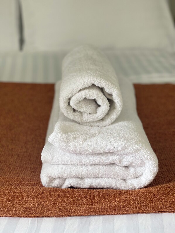 Una toalla blanca enrollada sobre una alfombra marrón texturizada, colocada en una cama blanca.