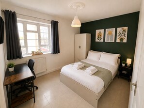 A bedroom with a bed, a desk, a chair, a radiator, a window with curtains, a wardrobe, and wall art. - Spacious 3BR/2BA – Central London - Walk to Paddington / Hyde Park (London)
