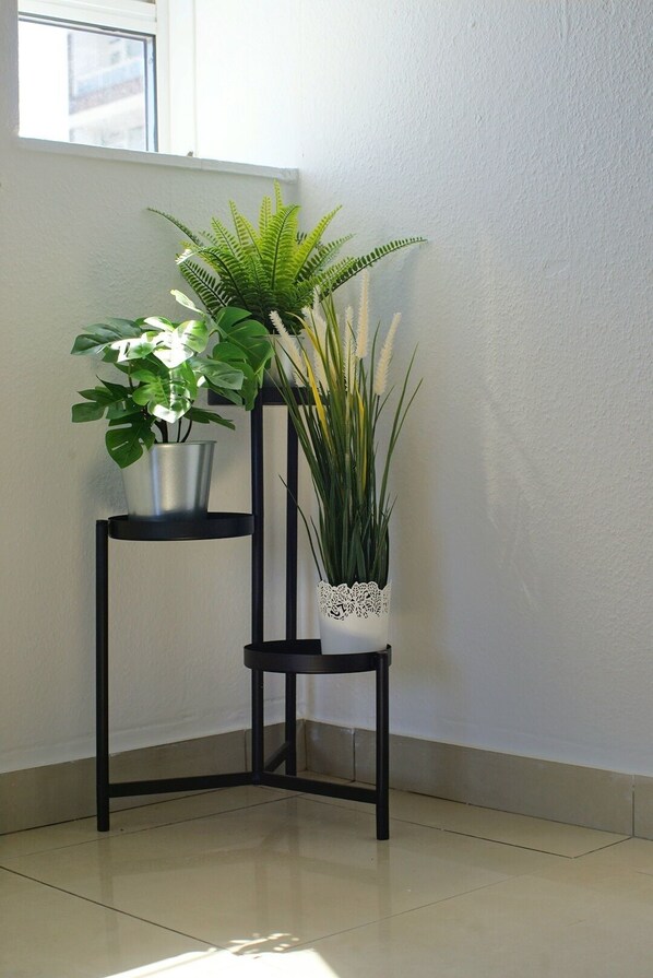 A corner with two black metal stands, each holding a potted plant.