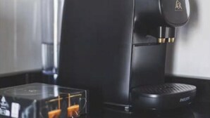 A black coffee machine with a digital display and a coffee pod holder on a reflective surface.
