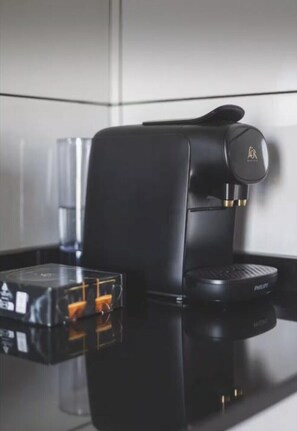A black coffee machine with a digital display and a coffee pod holder on a reflective surface.
