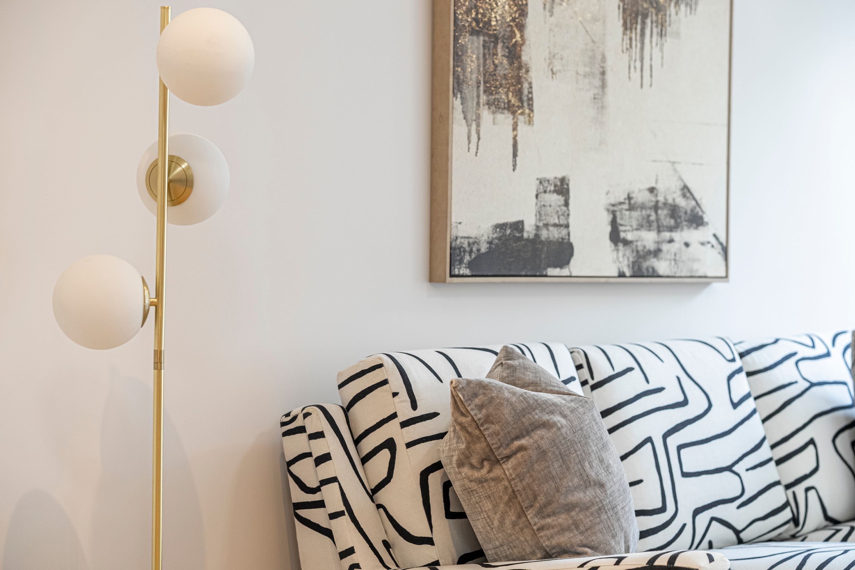A modern living room with a patterned sofa, a floor lamp, and a piece of abstract art on the wall.
