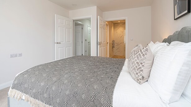 A bedroom with a bed, a patterned throw blanket, and a door leading to another room. - Quiet Luxe Escape 65s Only (Leatherhead)